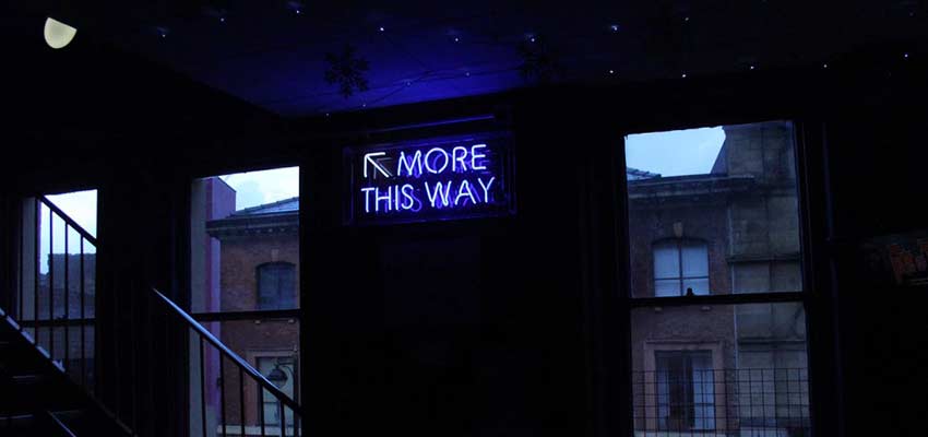 A neon sign that reads "More This Way".