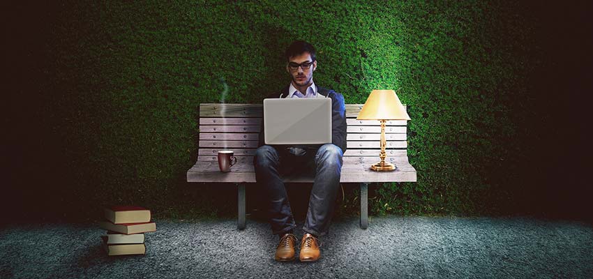 A man working on a laptop, while sitting on a park bench at night.