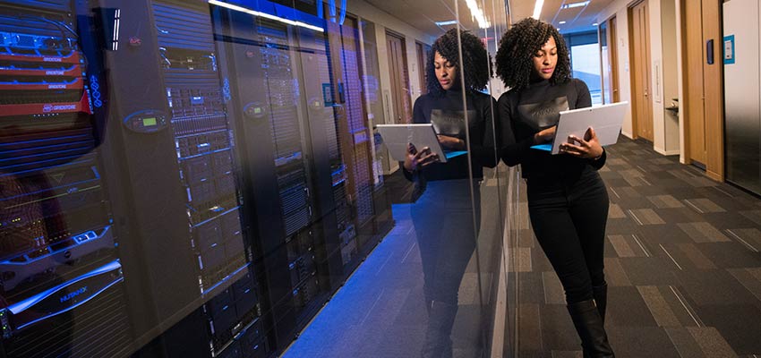 A woman using a laptop computer, standing near servers - Web Developer Skills