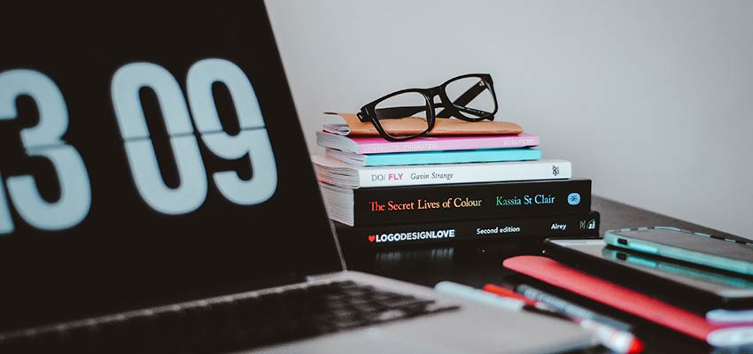 A desk with design books and a laptop computer - Web Developer Skills